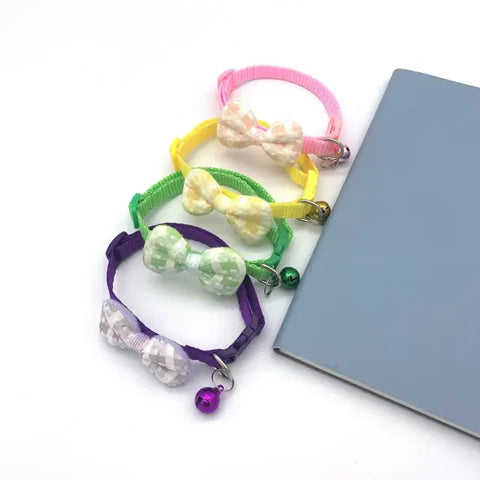 Colorful cat collars with bows and beads on a white surface next to a gray notebook.