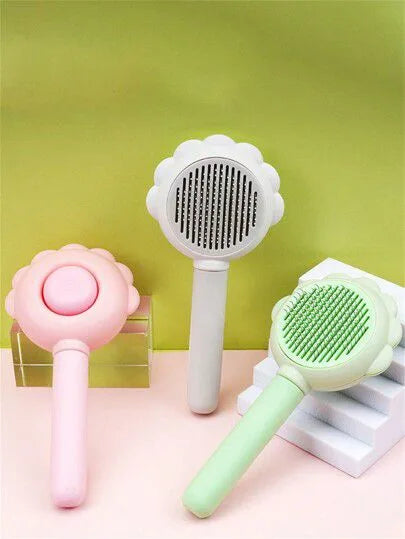 Three pet grooming brushes in pink, gray, and green on a pink surface with a green background.