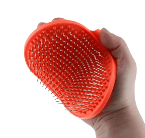 Hand holding a red pet grooming brush with metal pins on a white background
