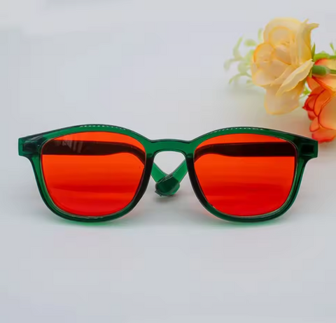 Sunglasses with red lenses and green frames on a light gray background with flowers.