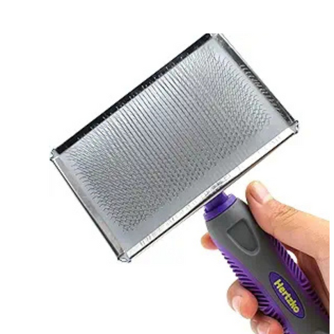 Hand holding a pet grooming brush with a purple handle on a white background